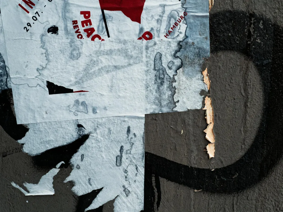 A wheatpaste poster aging on an urban wall